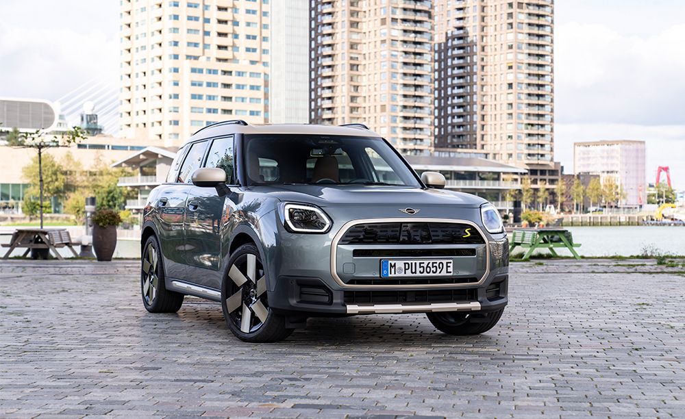 Ein eleganter grauer Mini Countryman S, geparkt am Wasser, mit modernen Gebäuden im Hintergrund